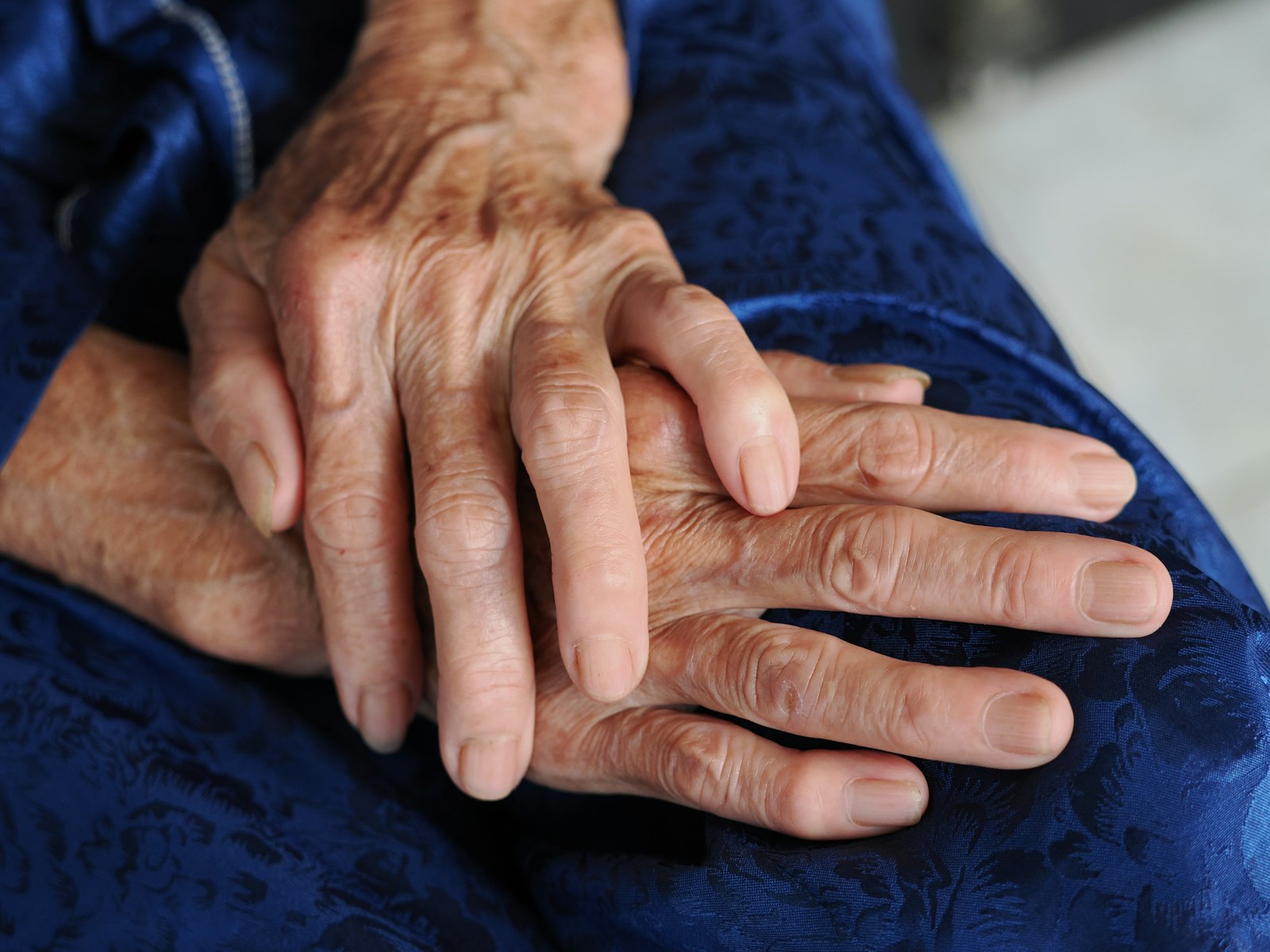 Close-up of elderly hands resting on a blue fabric