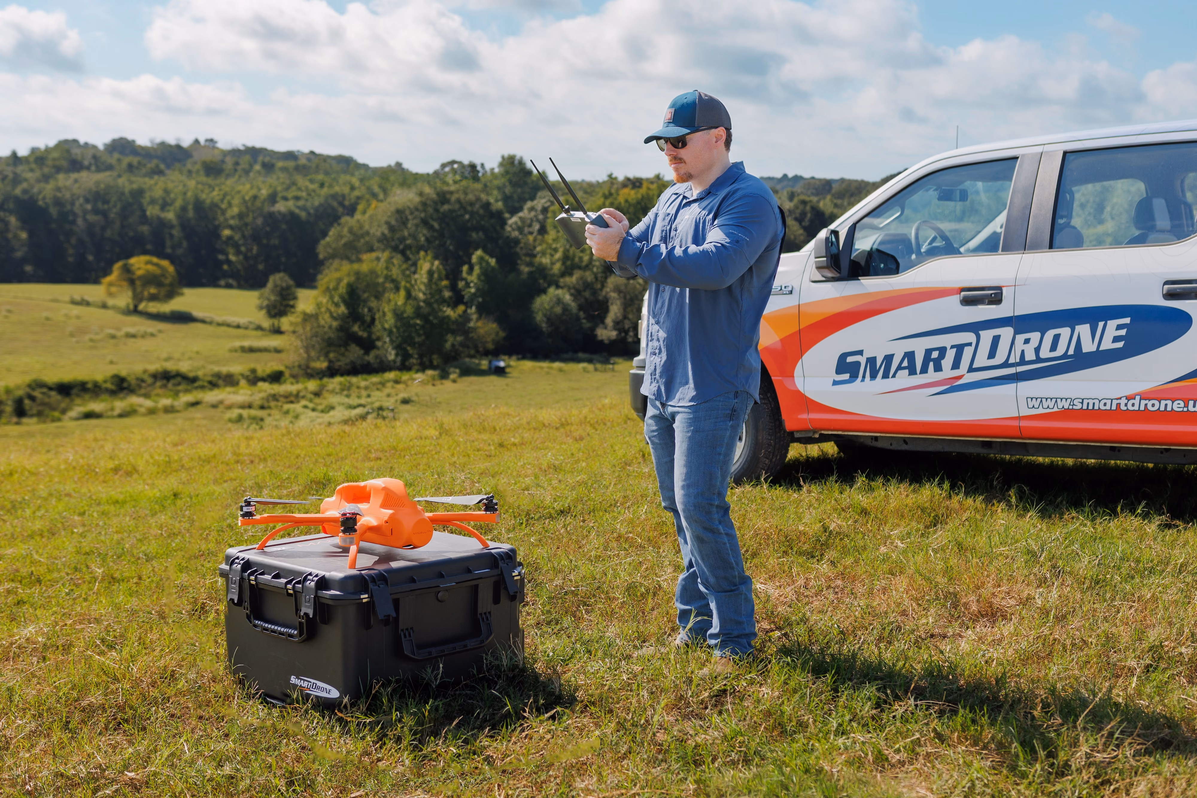 Person holding an orange Magellan drone outdoors with blurred natural background.