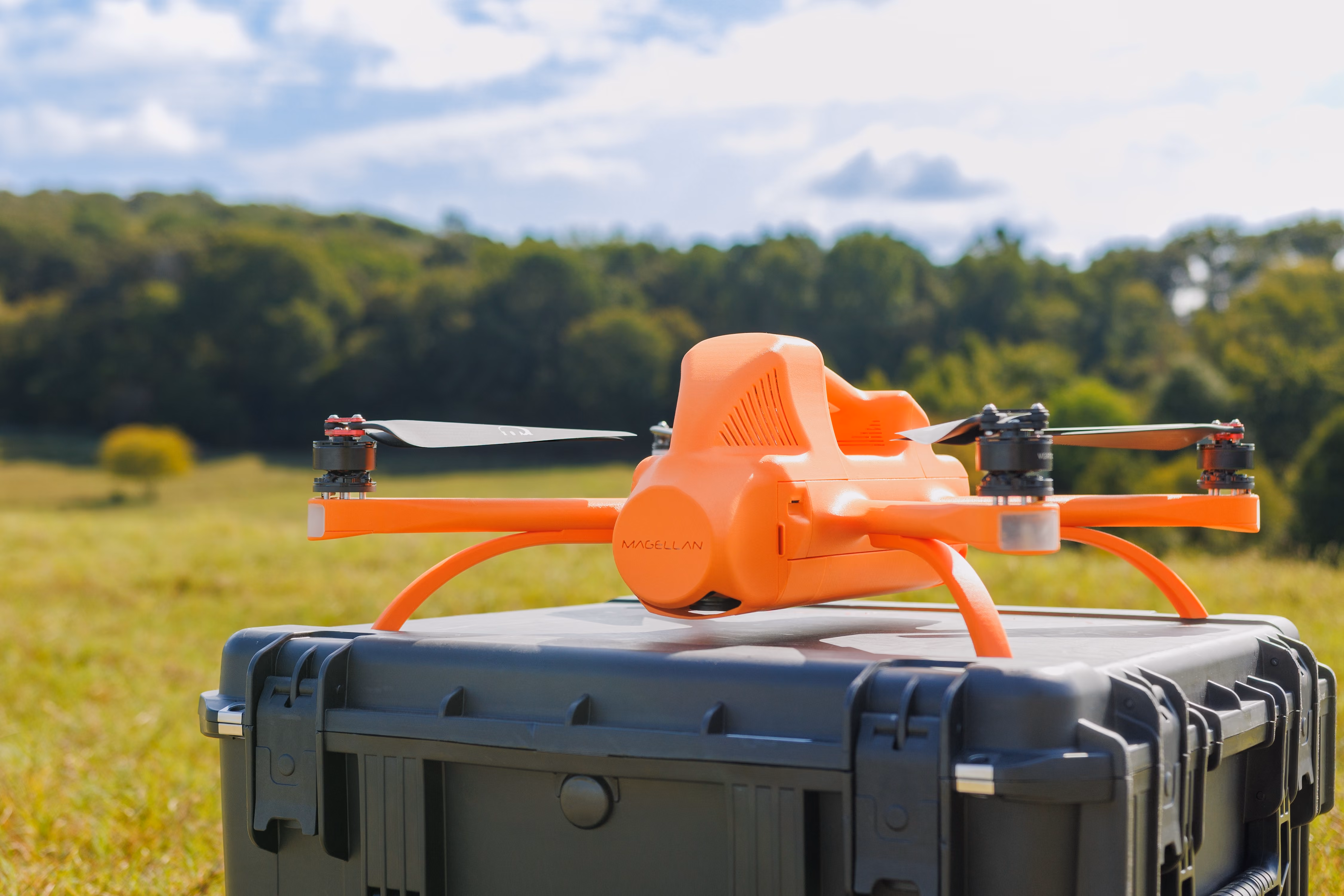 A SmartDrone Magellan surveying drone sits on its case while a land surveyor sets up a base station in the background