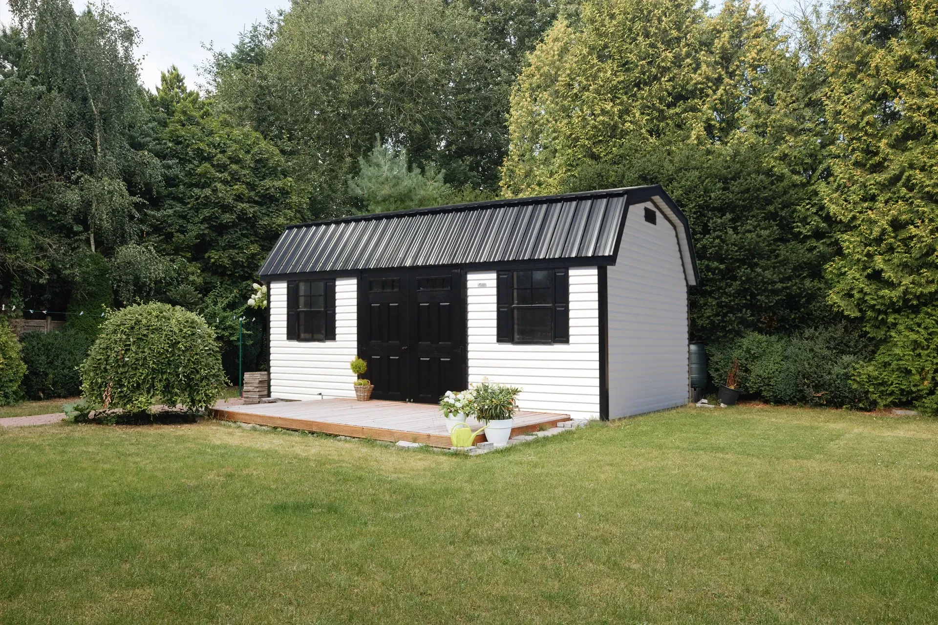The Richmond Shed with white siding, black doors and windows, and a black metal roof, with a small deck attached to the front.