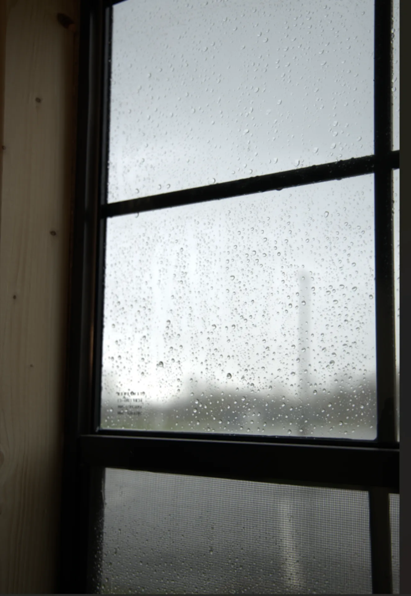 Close-up of a rain-covered windowpane with black framing and a screen below.