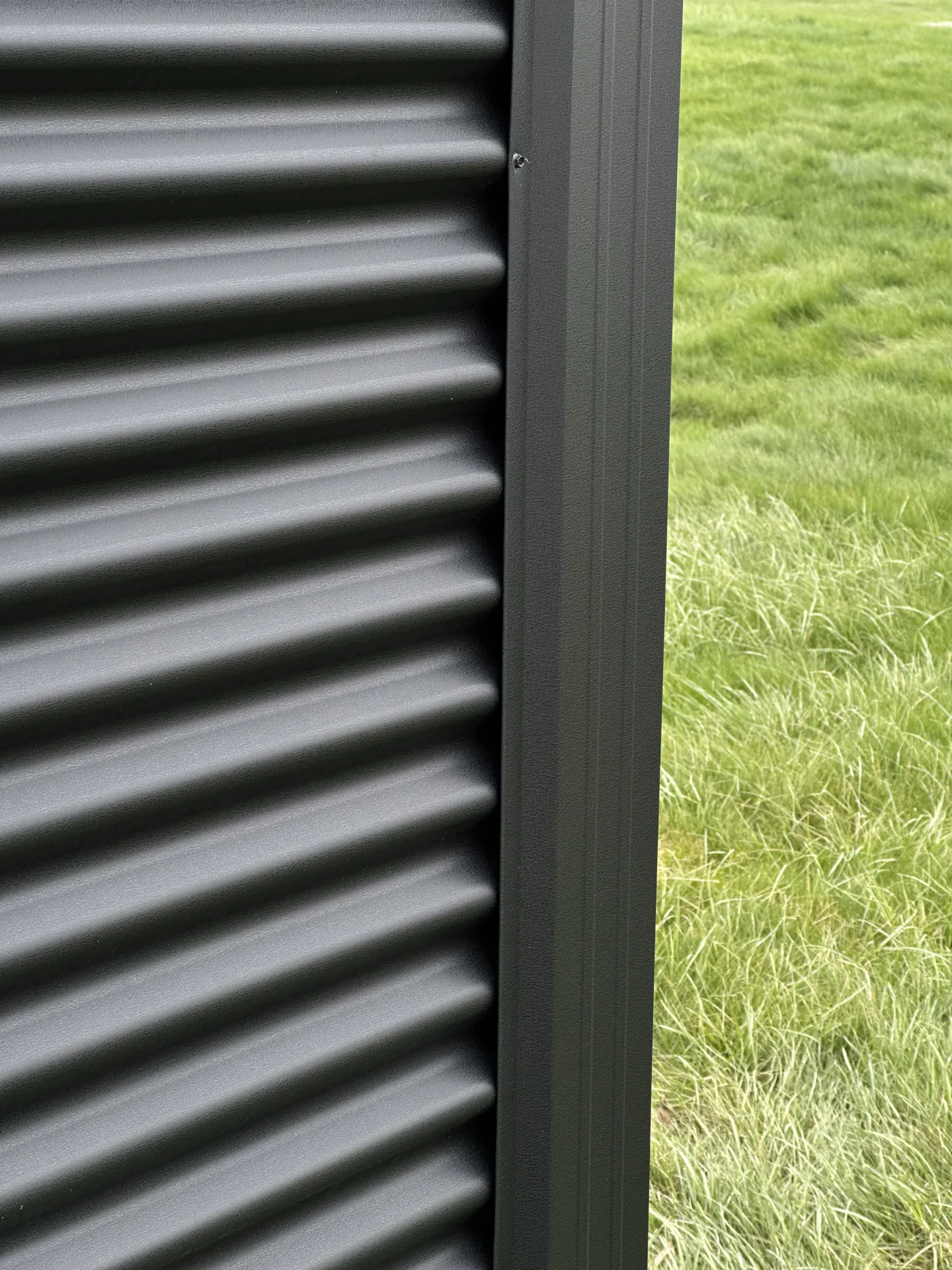 Close-up of modern dark gray corrugated metal siding with green grass in the background.