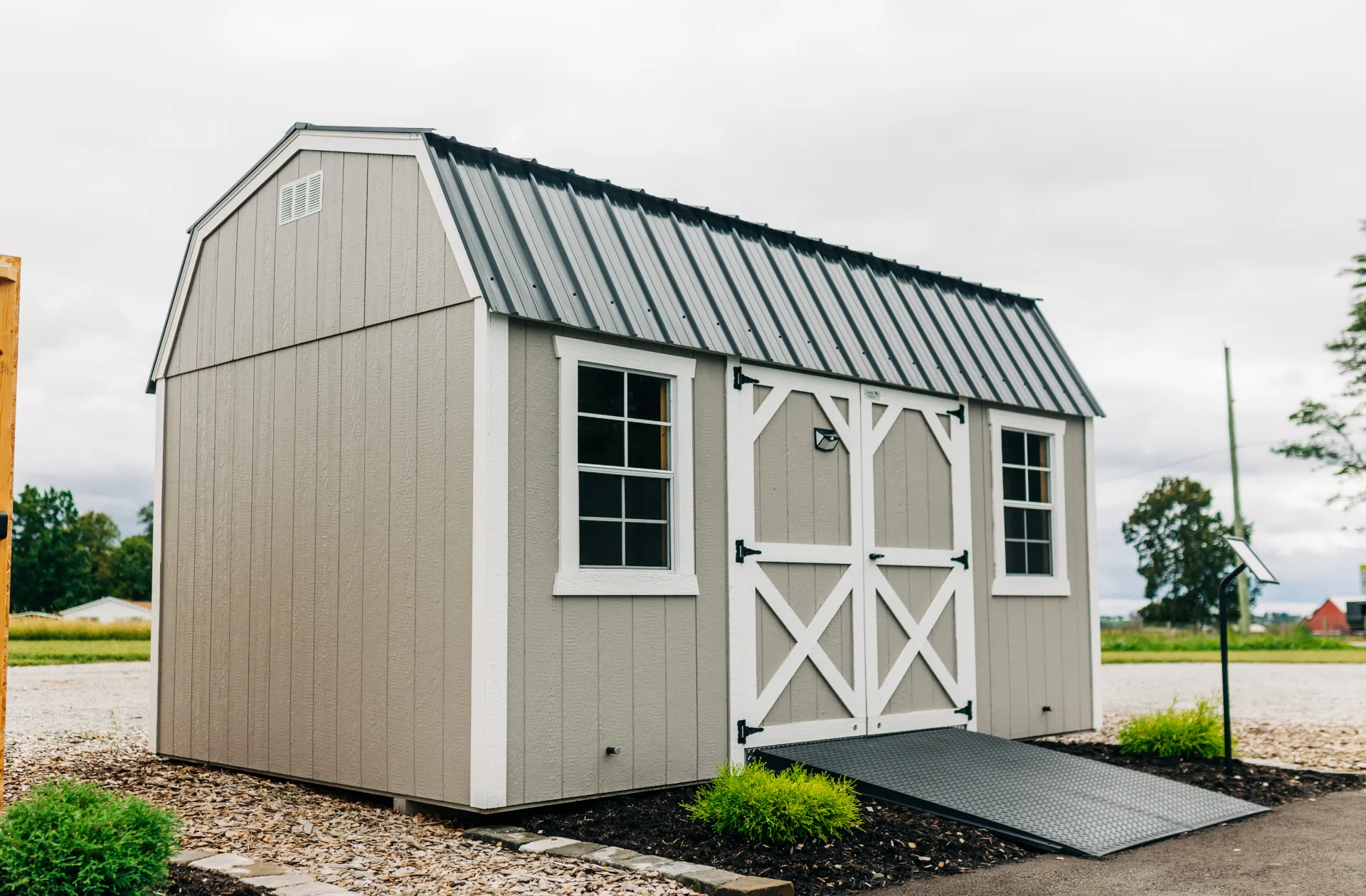 Tan storage shed with white trim, metal roof, double doors, ramp, and two windows on sides.