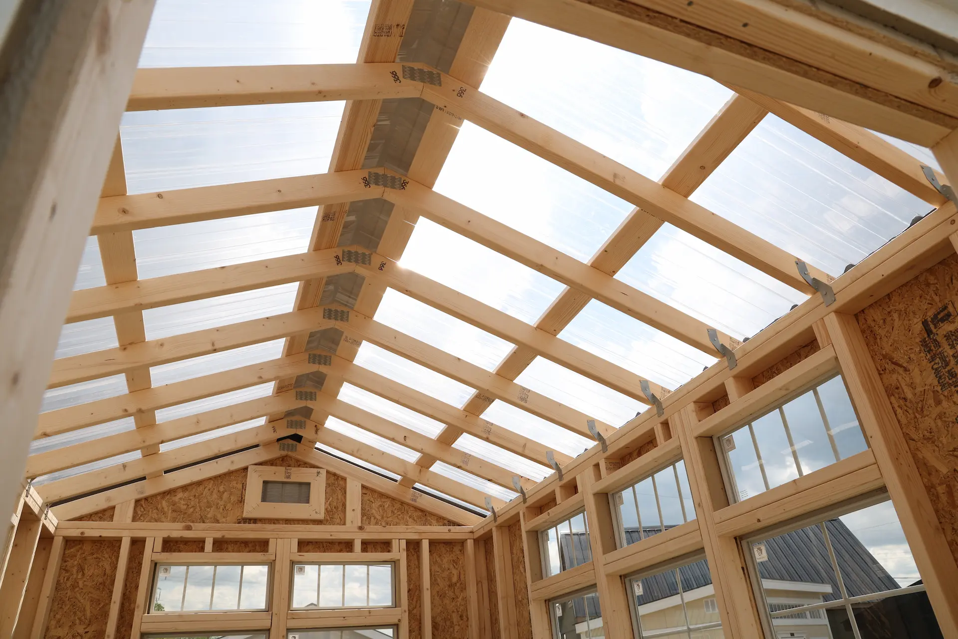 Interior view of a wooden-framed shed with transparent roof panels and window frames.