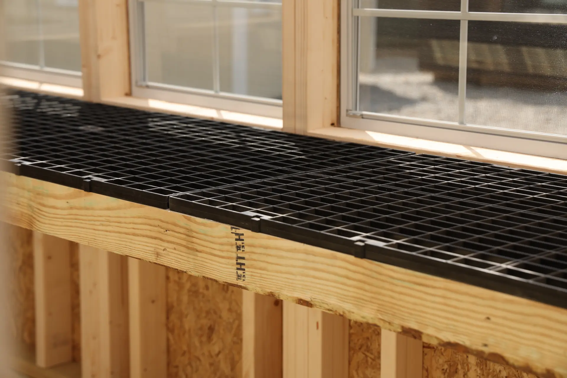 Black plastic grid trays on a wooden potting table beneath greenhouse windows.