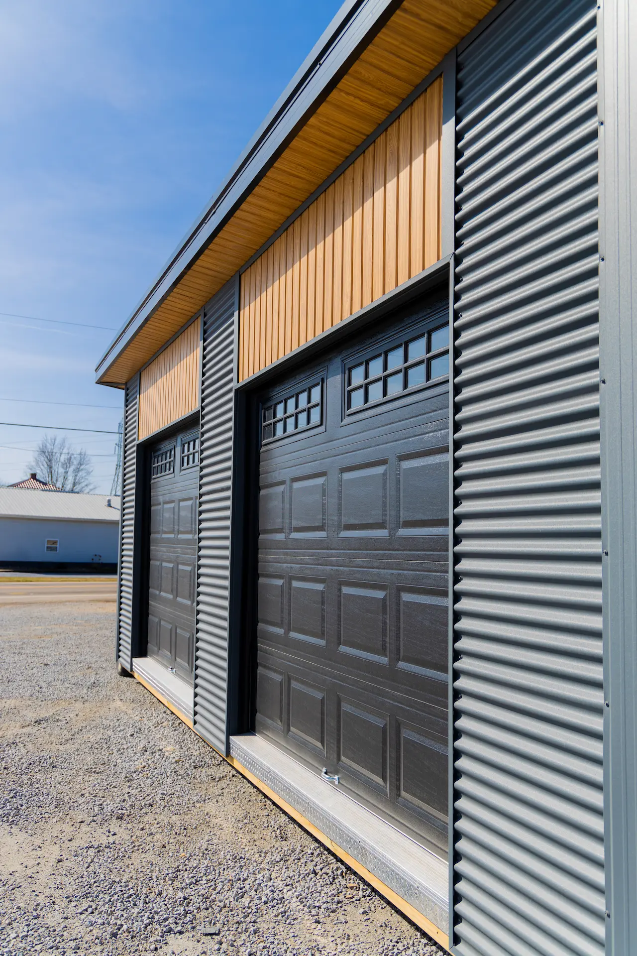Modern shed with two black garage doors and corrugated metal siding with wood panels above.