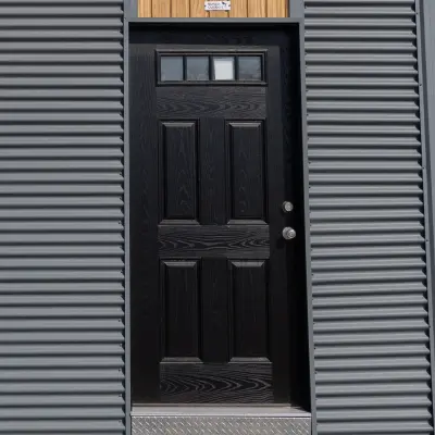 Black exterior door with six panels and a horizontal window at the top, set in gray corrugated siding.