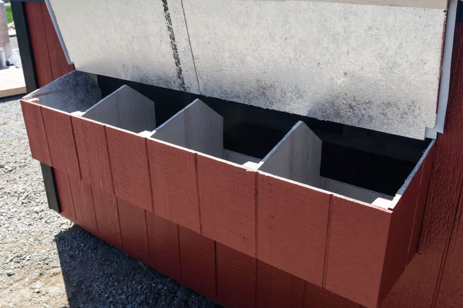 Open wooden nesting box with four compartments attached to a red exterior wall outside.