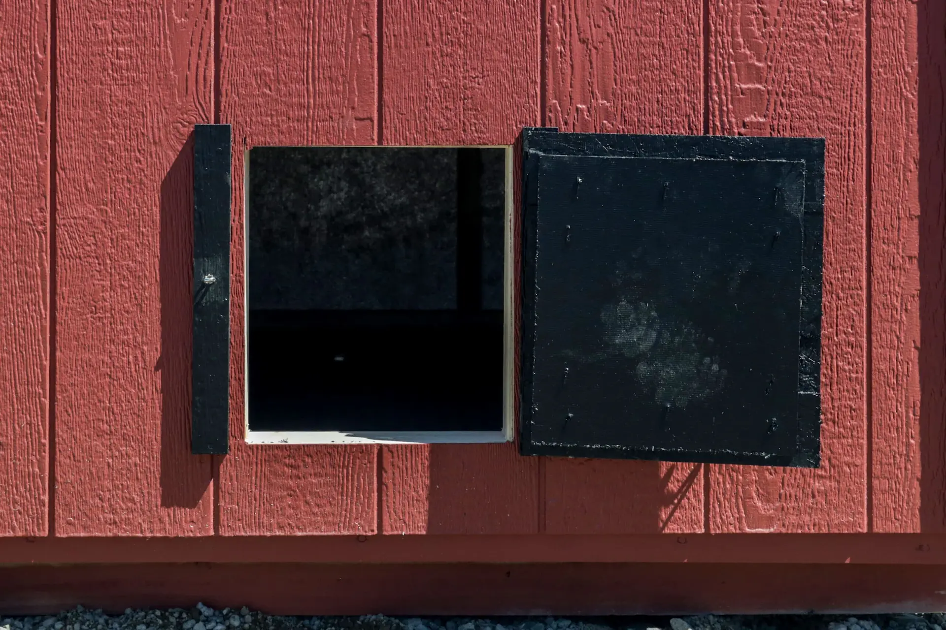 Open black square hatch on a red wooden wall showing a dark interior space.