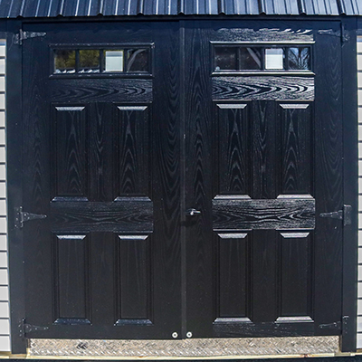 Black wooden double door with rectangular windows at the top set in a building with metal siding.