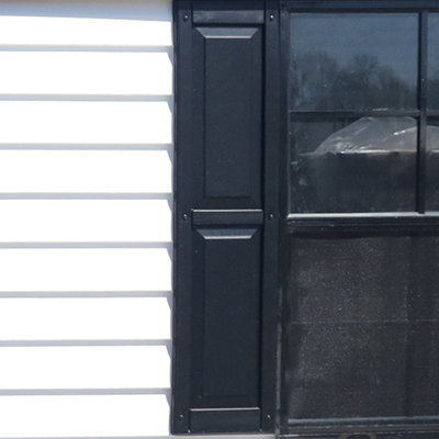 Close-up of a black decorative shutter next to a window with white siding on a house exterior.