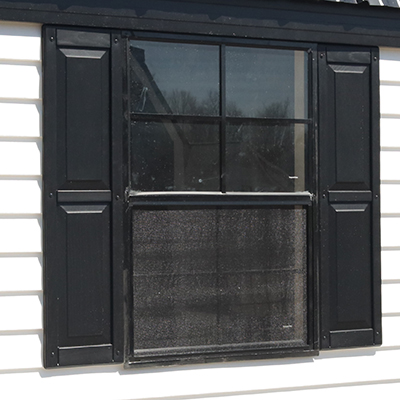 Black framed window with black shutters on white siding of a shed