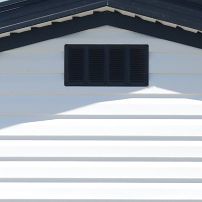 Close-up of a black air vent on white siding beneath a dark roof overhang.