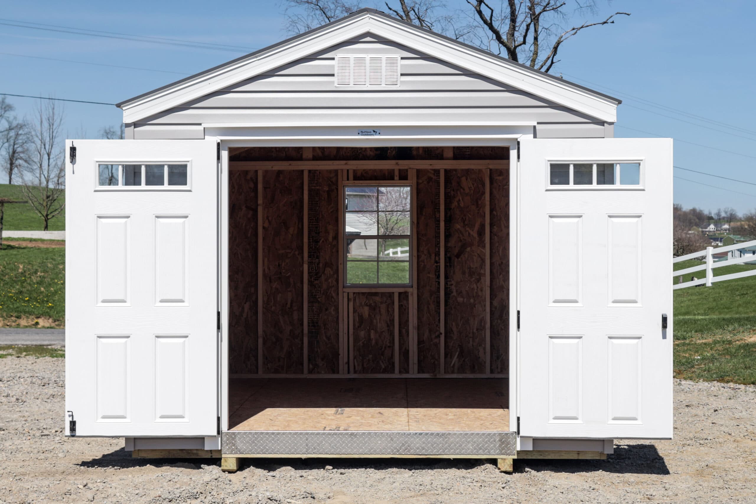 White storage shed with double doors open showing unfinished wooden interior and a window inside.