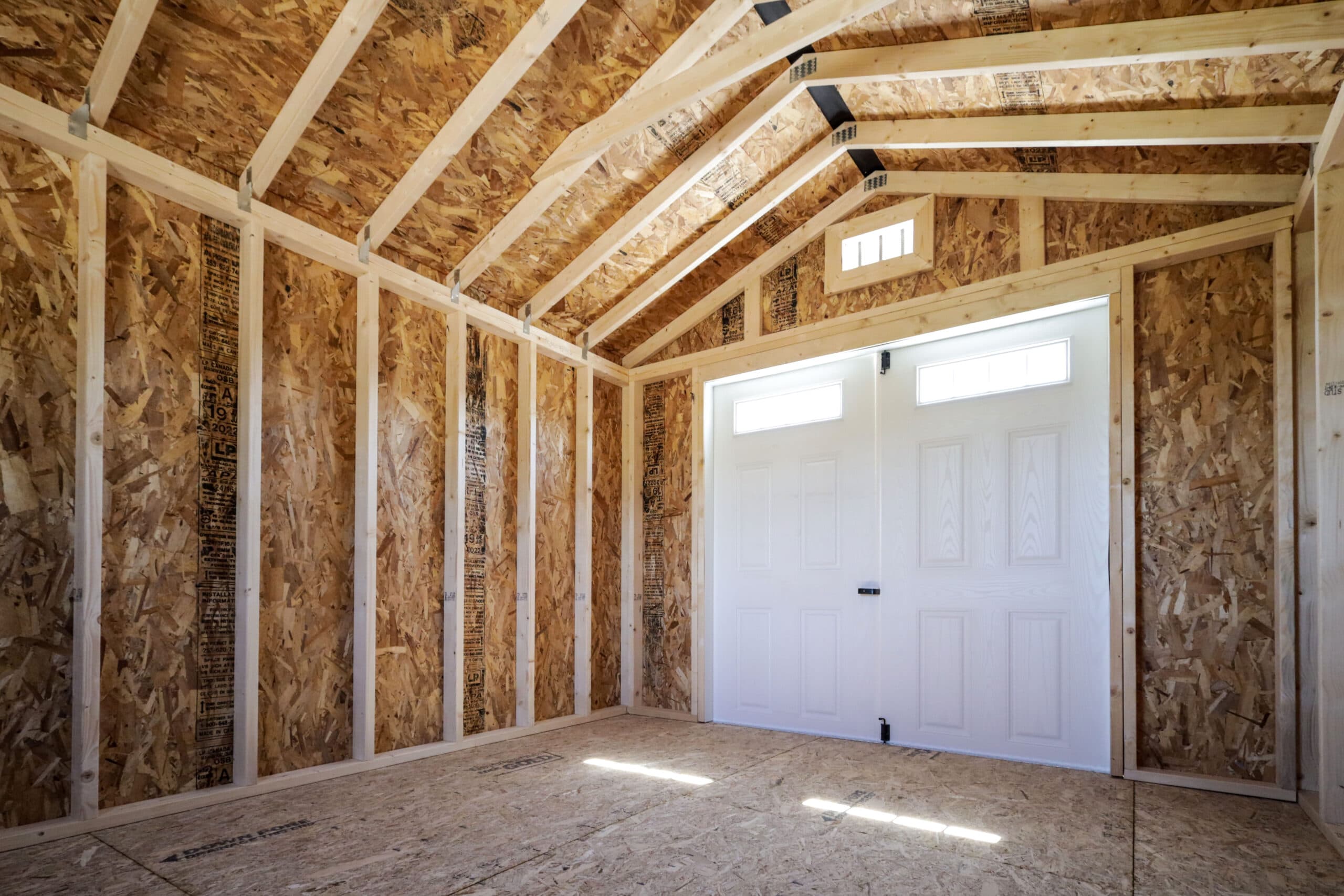 Empty wooden shed interior with exposed plywood walls, ceiling, and double white doors with small windows.