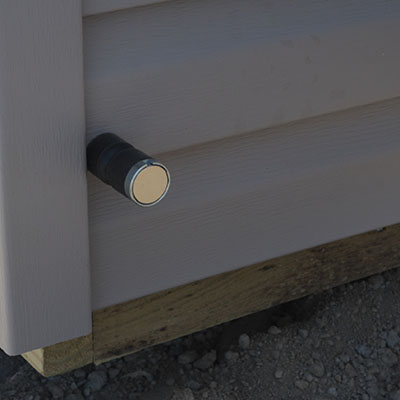 Close-up of a metallic magnetic door stop attached to an exterior wall with siding.