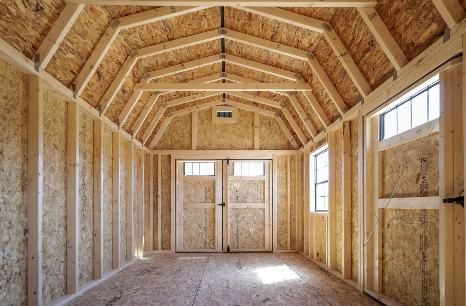 Empty interior of wooden framed shed with two windows and a double door at the far end.