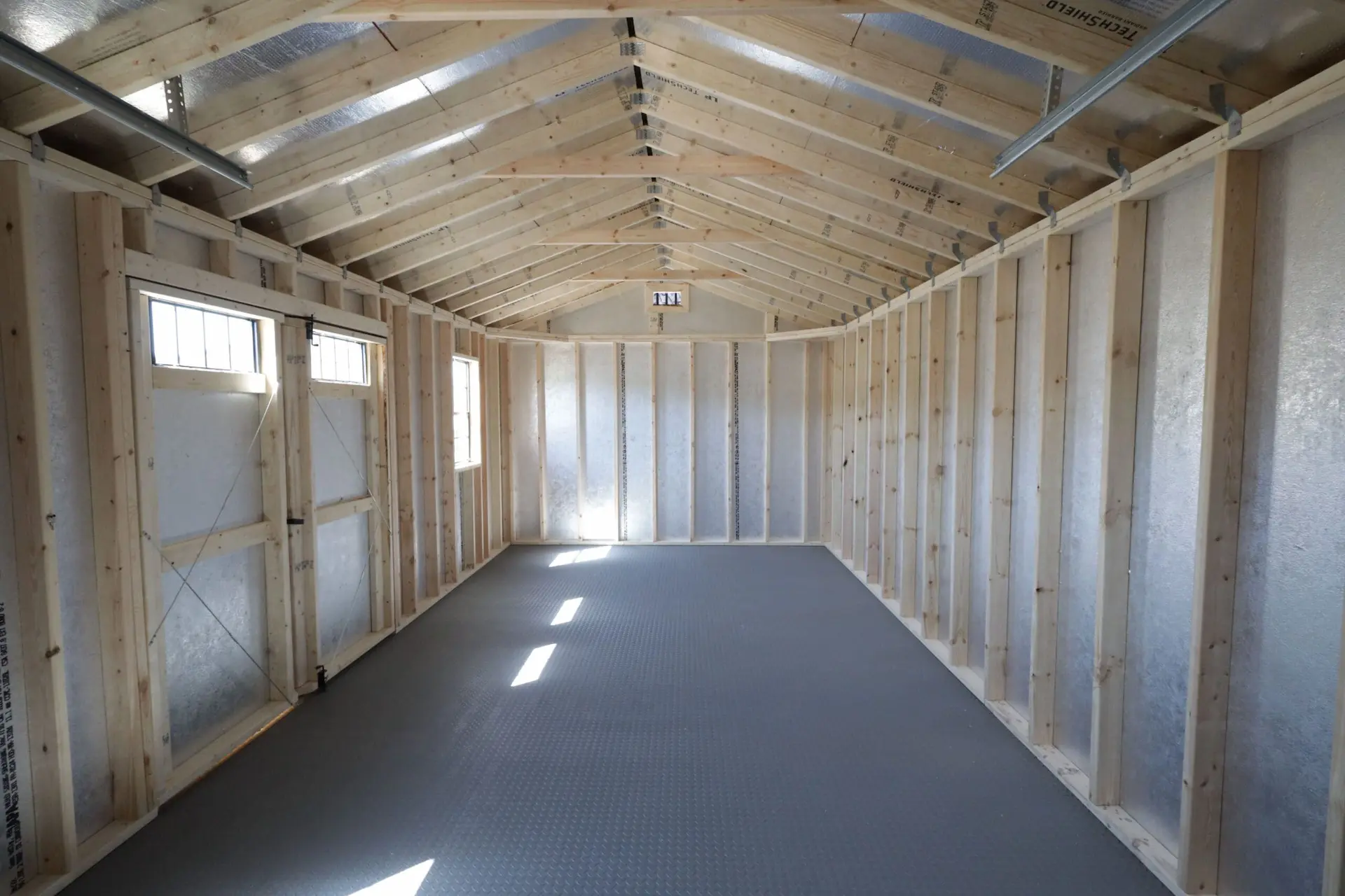 Interior of an empty wooden frame shed with a gray floor and exposed roof trusses.