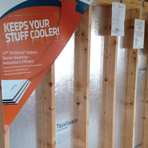 Wall studs with reflective TechShield radiant barrier panels installed behind them in a building frame.