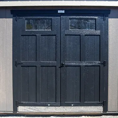 Black double wooden doors with small rectangular windows at the top on a beige building.