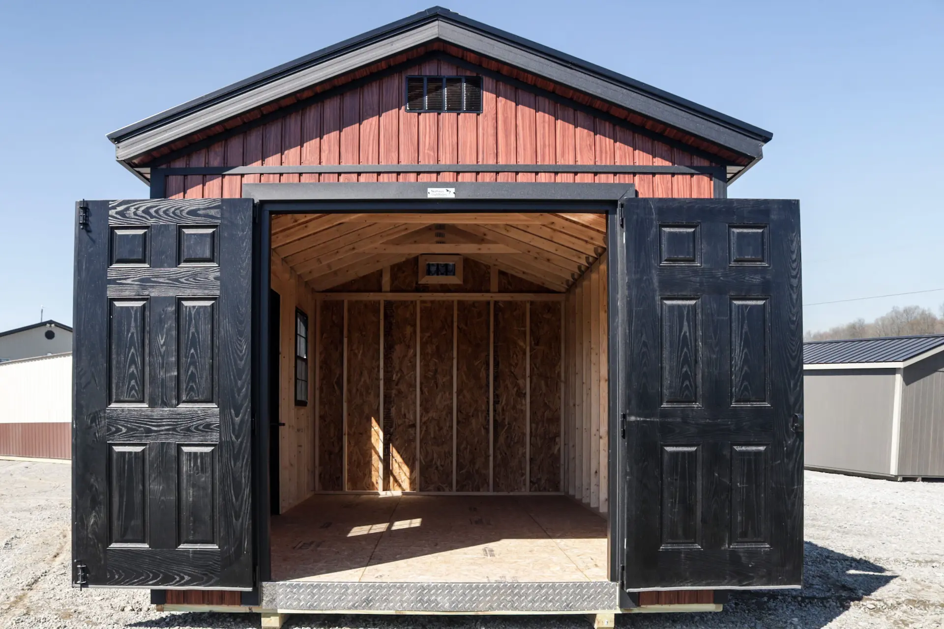 Empty wooden shed with open black doors under clear blue sky.