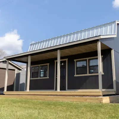 Modern small dark house with a metal roof and a wooden porch under blue sky.