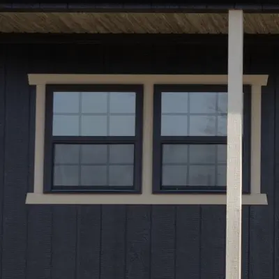 Two black-framed windows with grid patterns set in dark wooden wall next to a white vertical post.