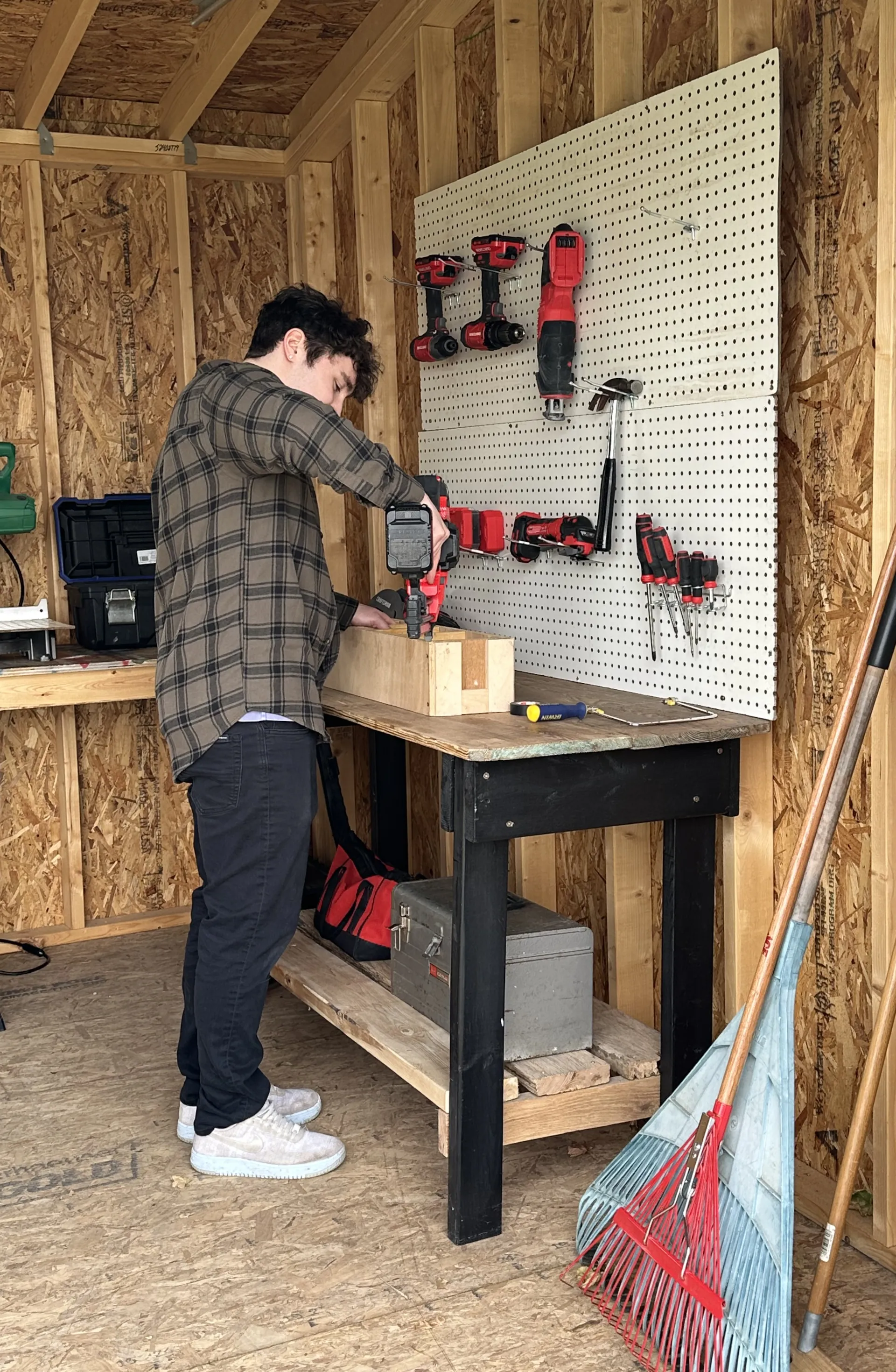 man using a nail gun on a wooden structure, with tools hanging up on a pegboard