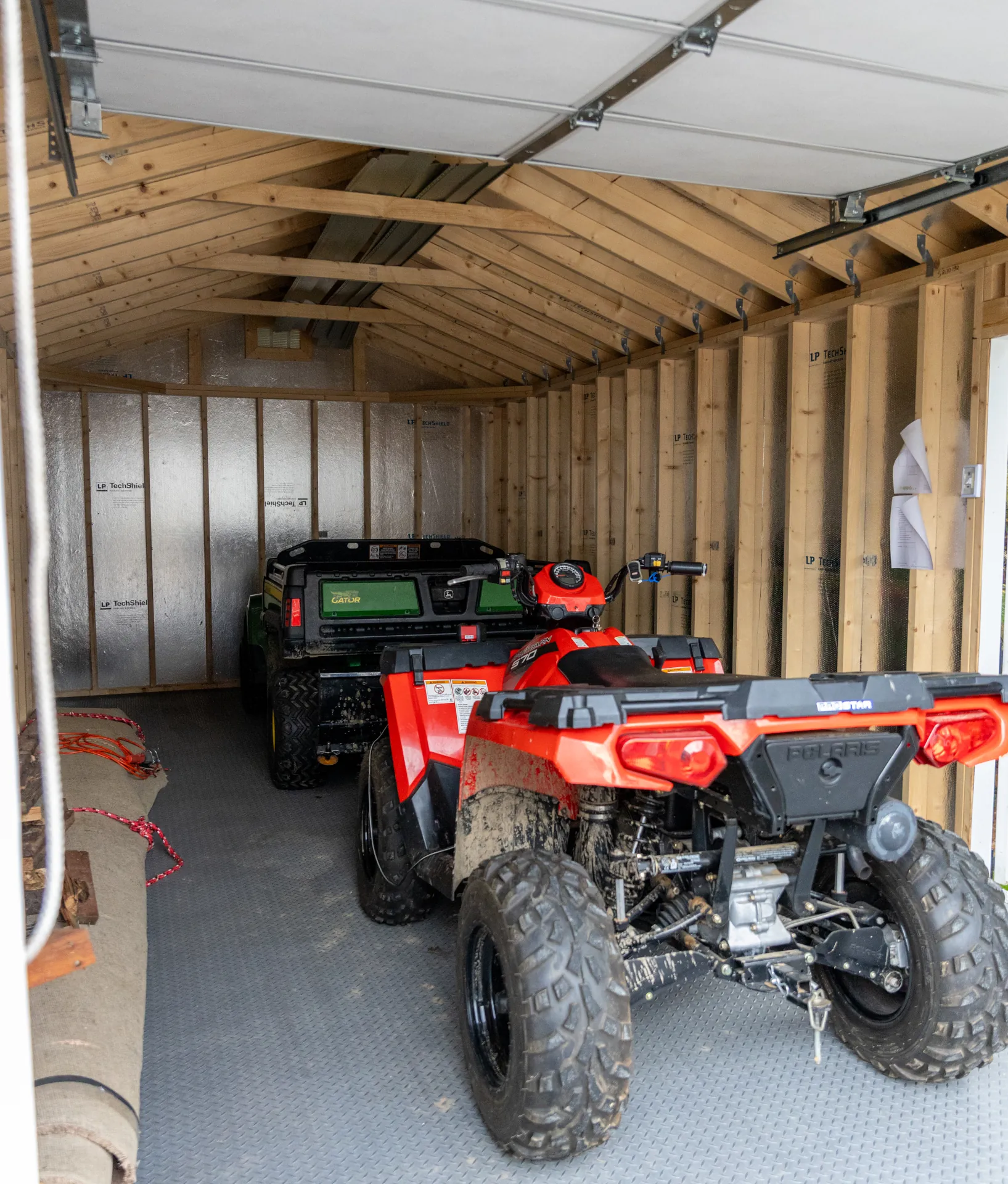Interior of a wooden garage with an ATV and utility vehicle parked inside.