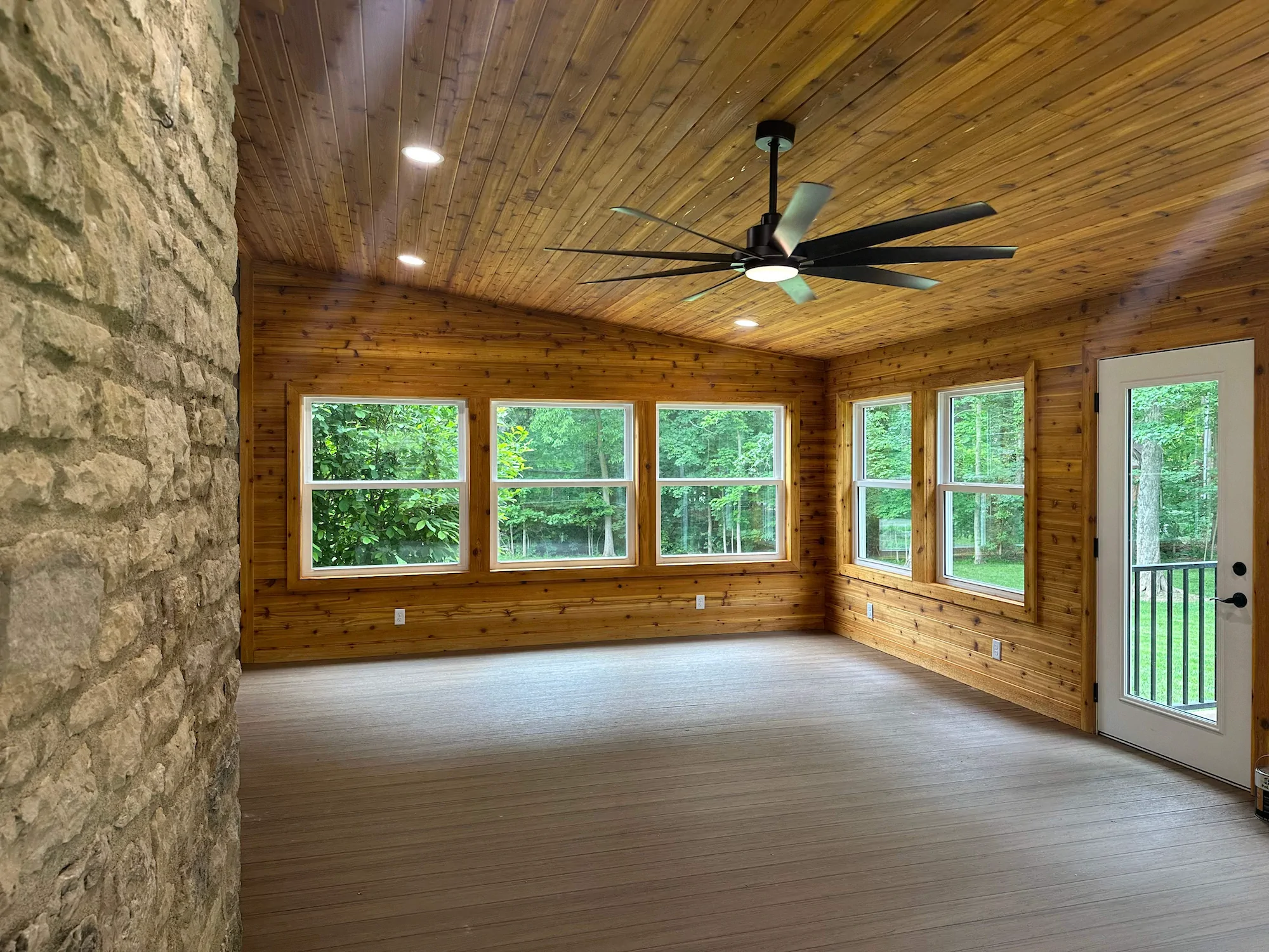 The natural wood interior of a gorgeous sunroom conversion with a large ceiling fan.