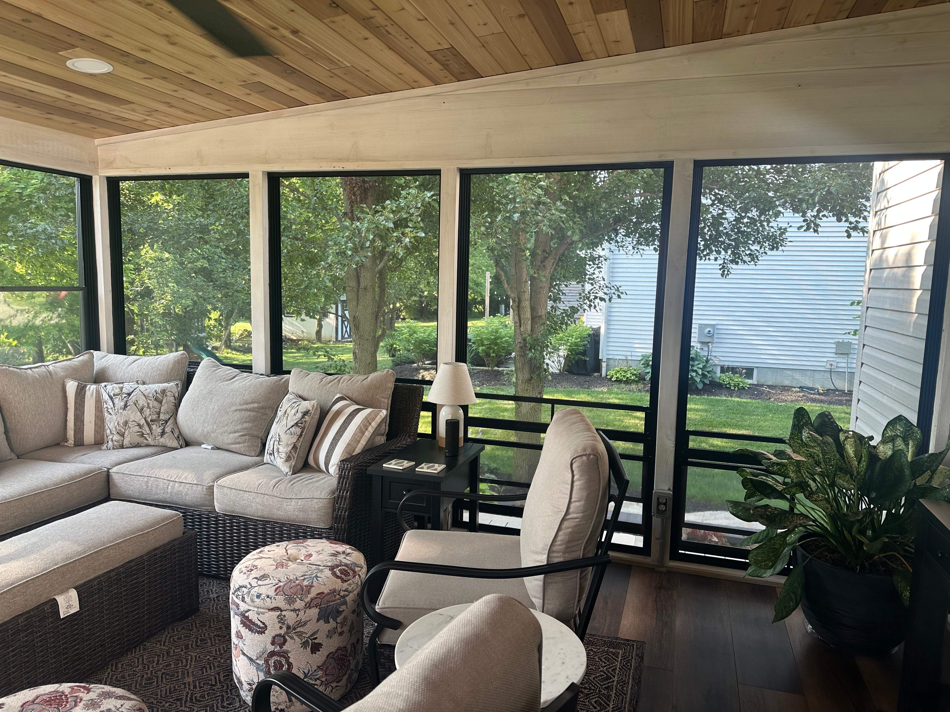 A screened-in porch with a potted hosta, EzeBreeze windows, and sunroom furniture.