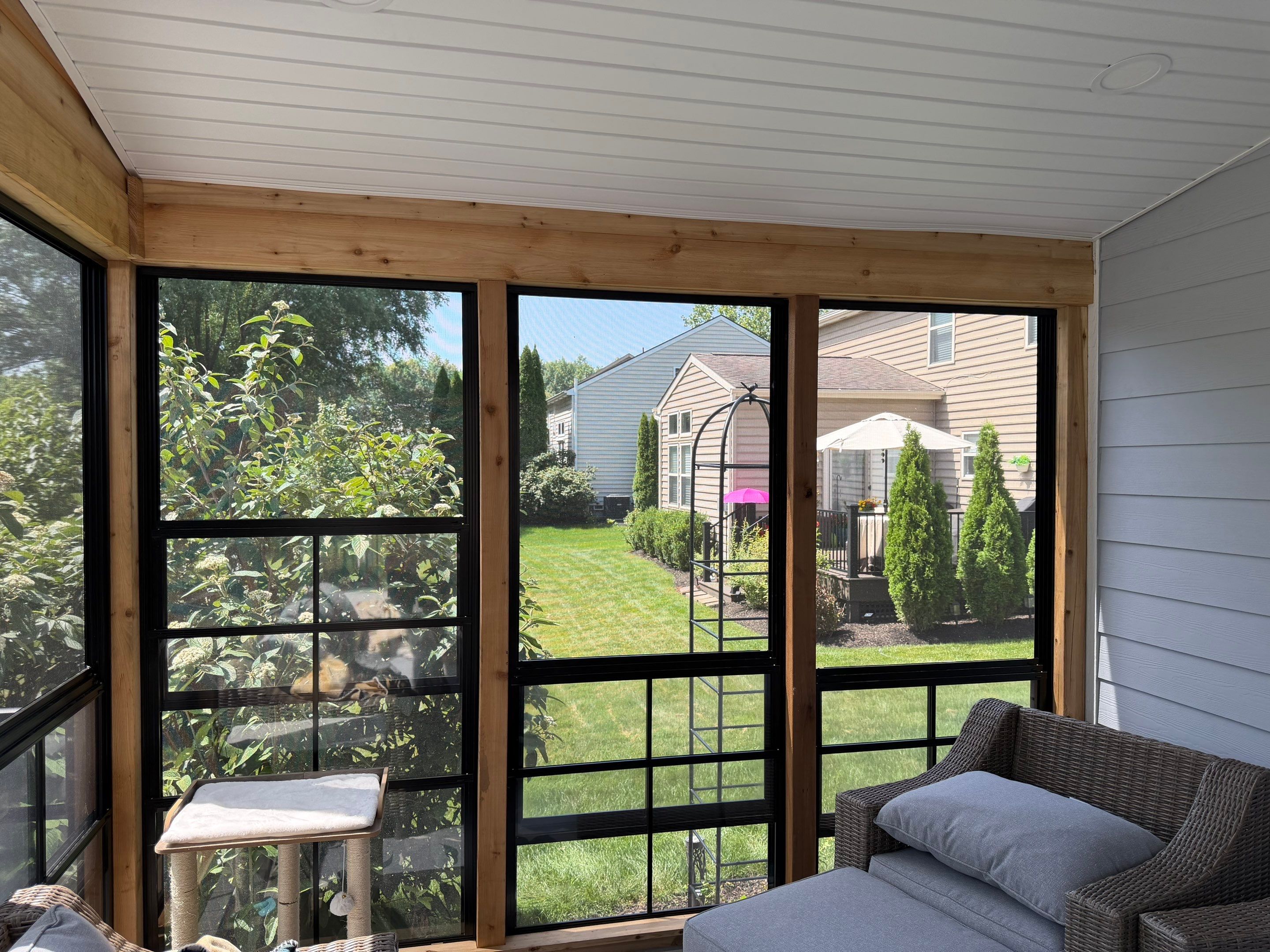 An enclosed porch with vertical four-track windows, a matching ottoman and chair combo, and a cat tree.