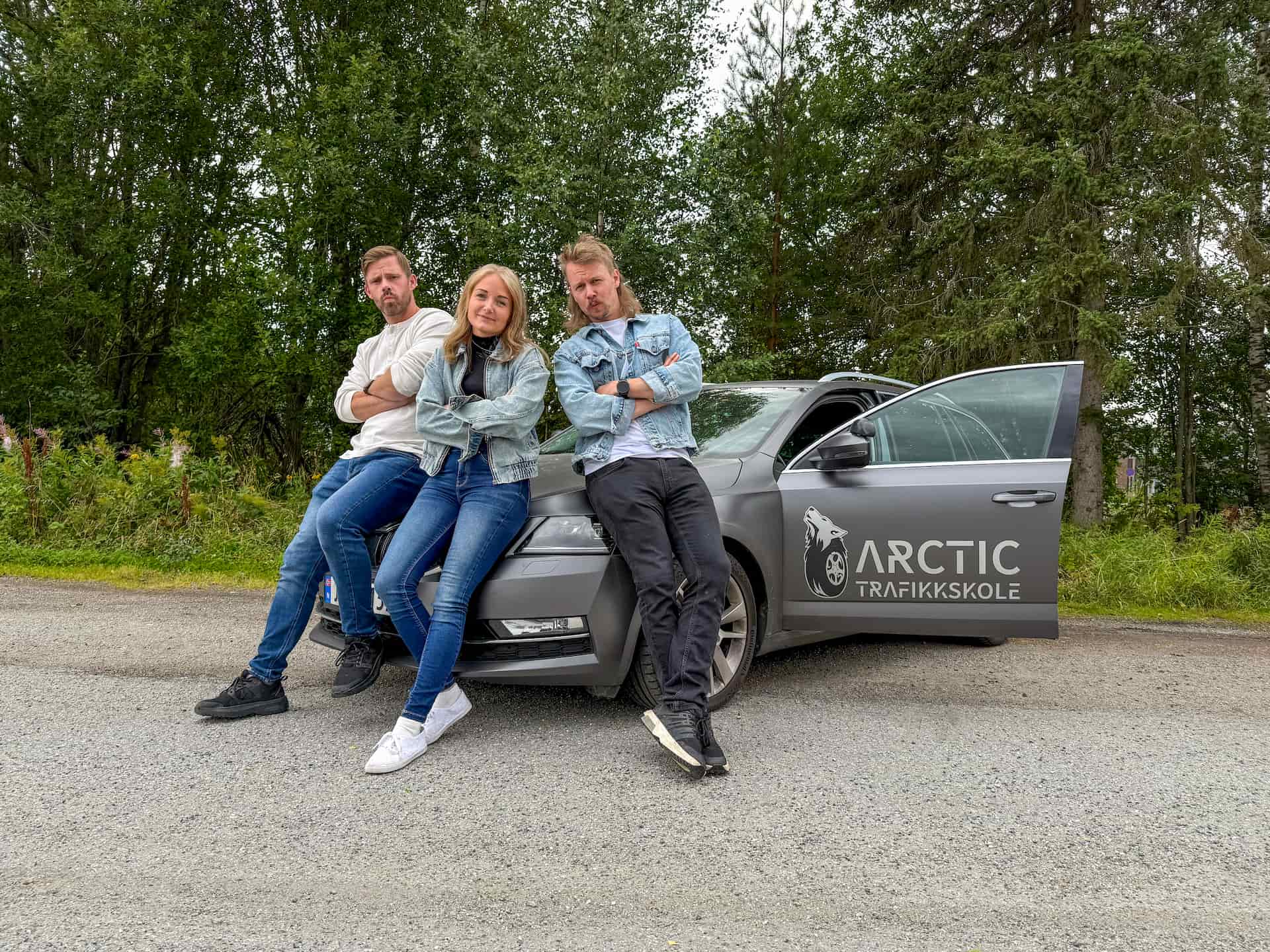 Tre ansatte hos Arctic Trafikkskole som poserer foran en kjøreskole-bil