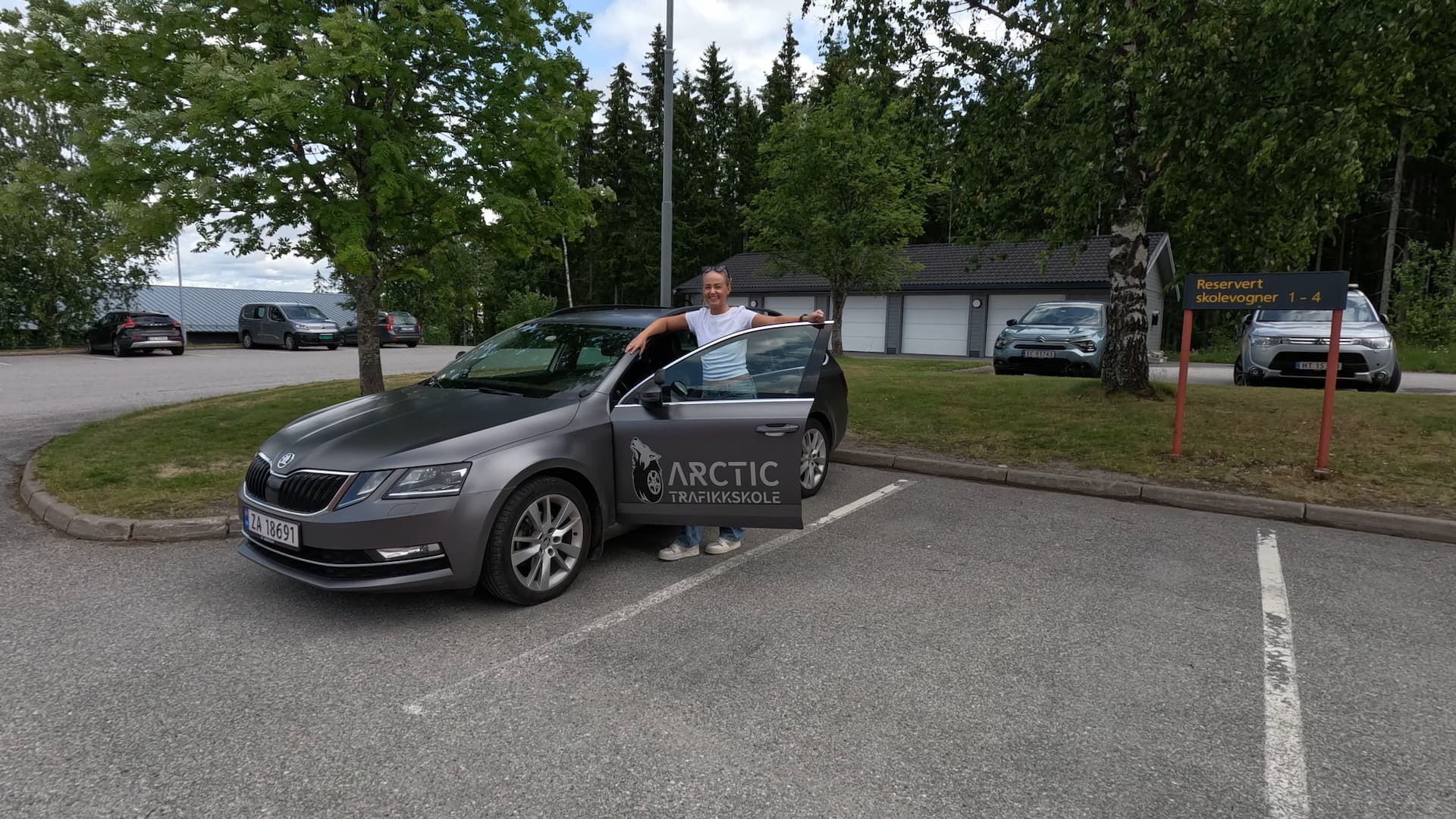 En blid og glad elev hos Arctic Trafikkskole som poserer med kjørekole-bilen