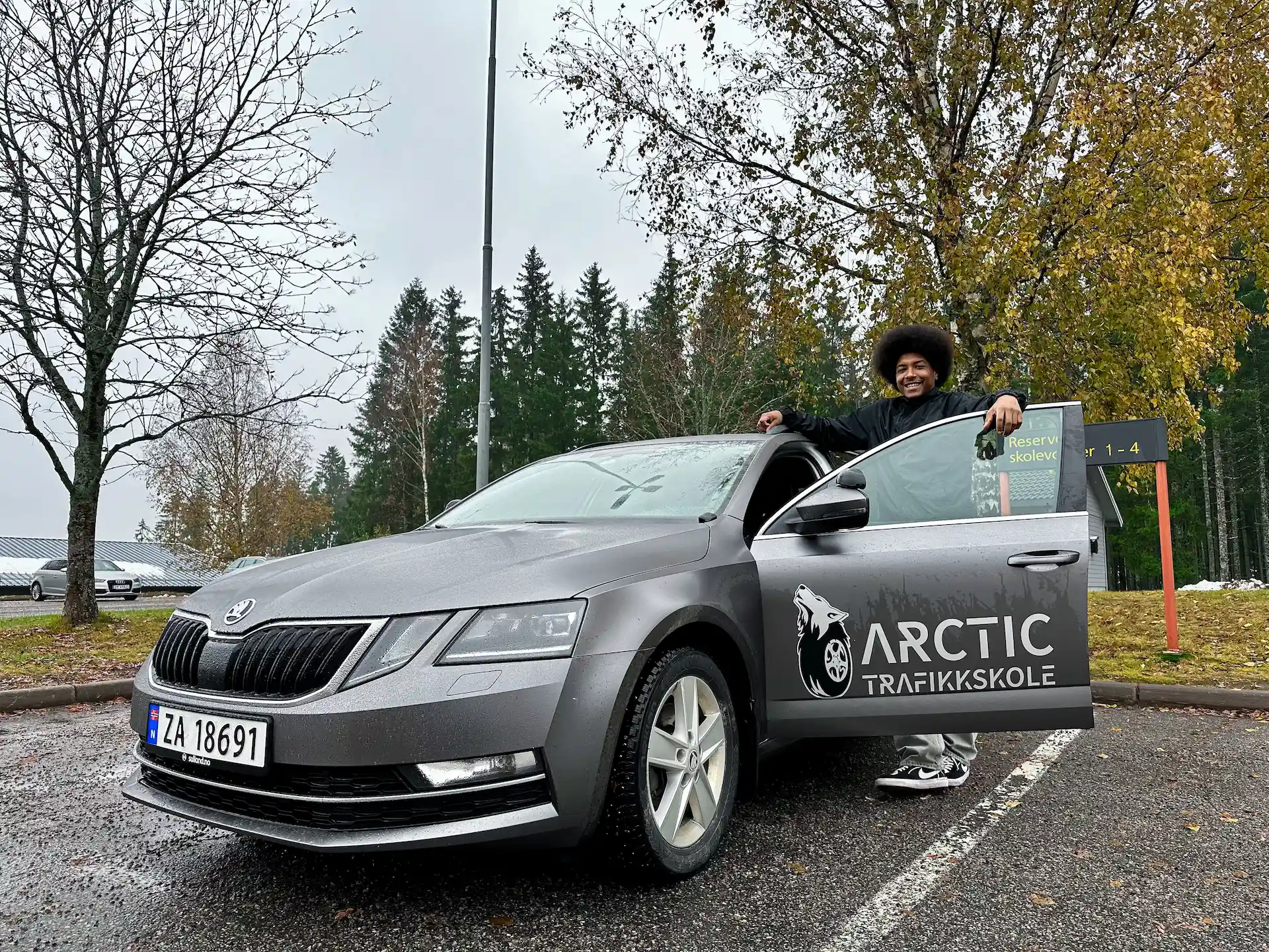 En fornøyd elev poserer med kjøreskole-bilen og er klar for kjøretime