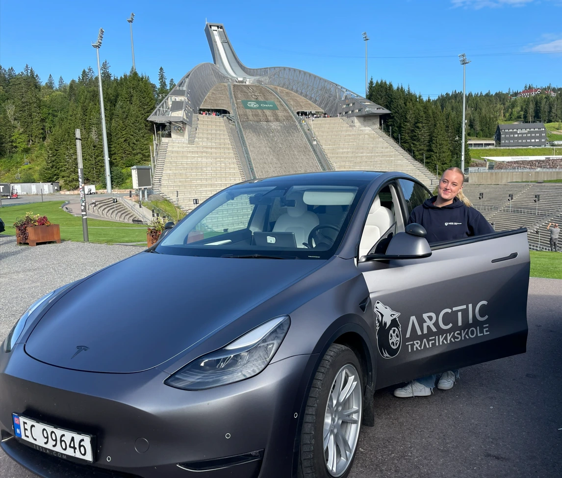 En blid elev poserer med kjøreskole-bilen foran Holmenkollen