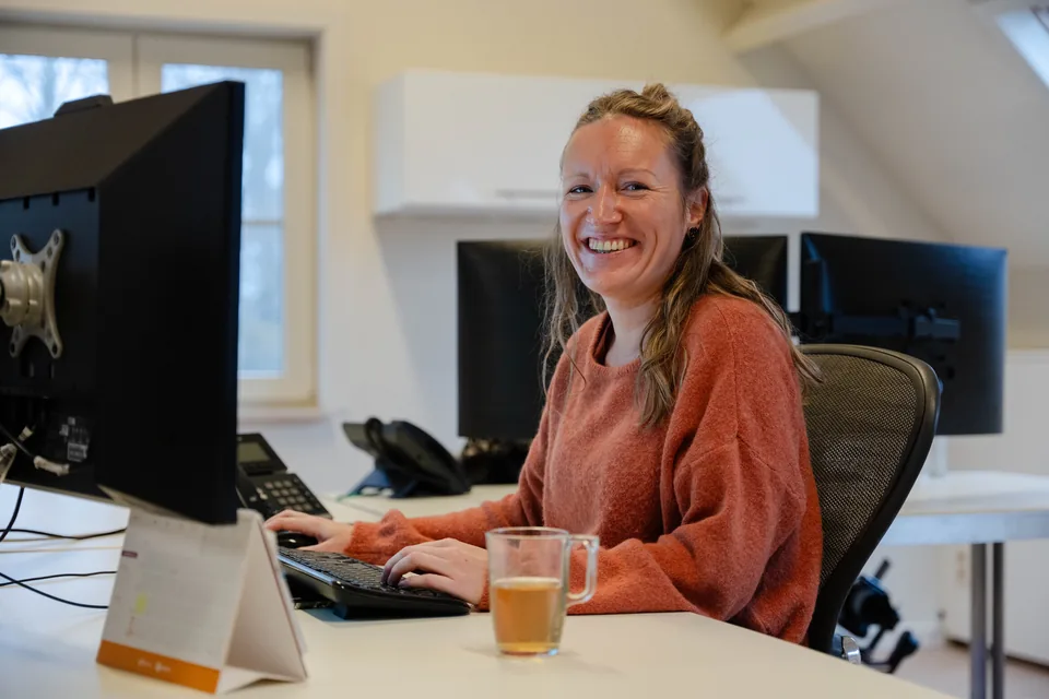 Een lachende collega van Meesters aan haar bureau op kantoor