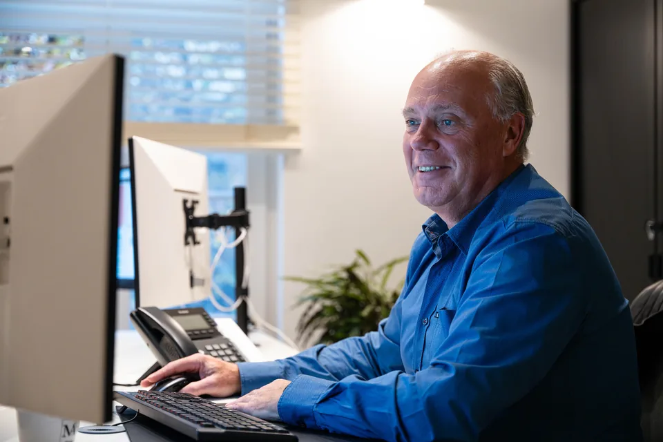 Medewerker werkt glimlachend achter zijn computerscherm