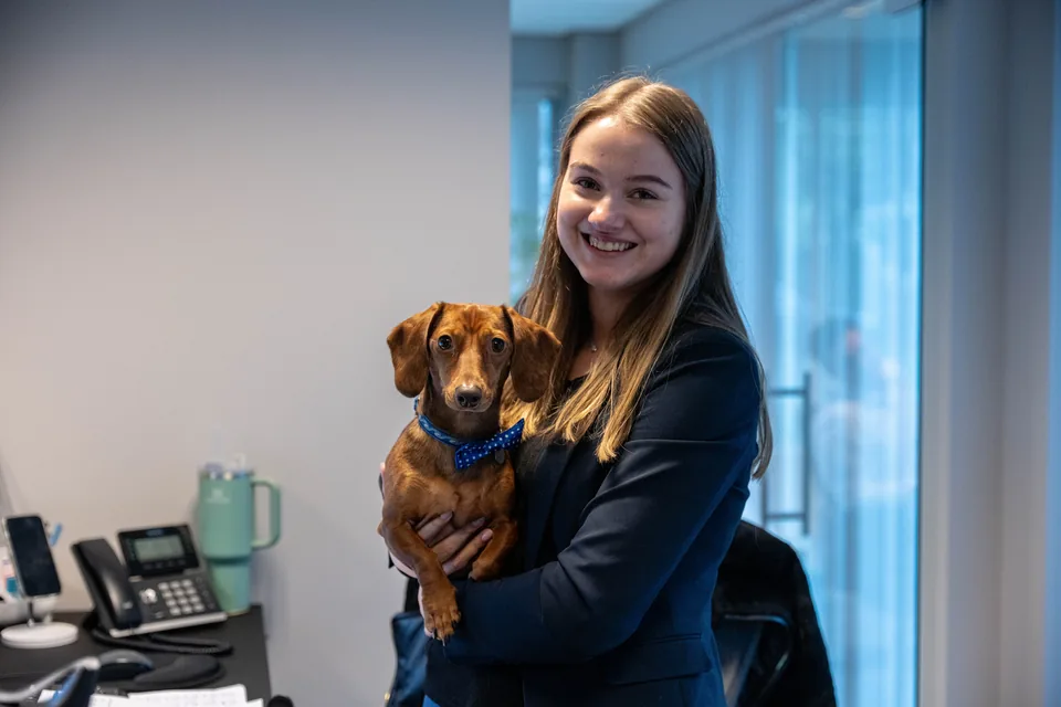 Medewerkster houdt lachend de kantoorhond vast, een teckel met strikje
