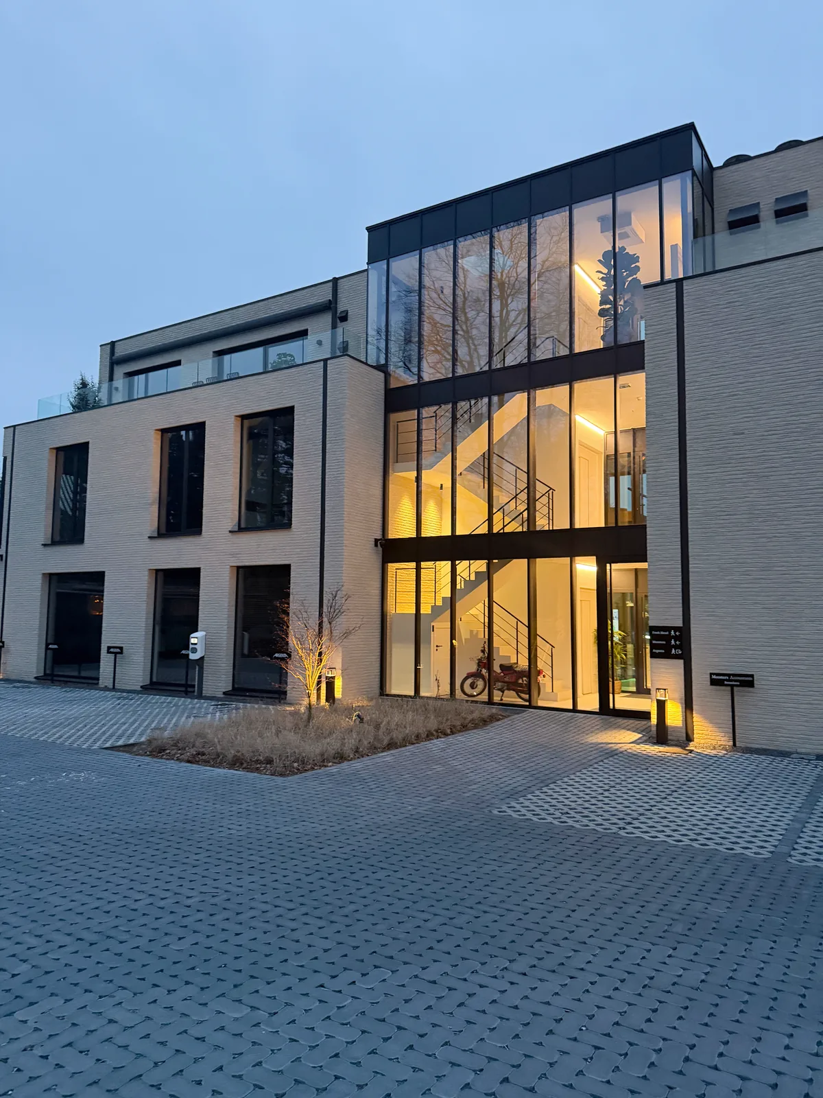 De verlichte glazen inkom en gevel van het kantoor in Schilde bij avond