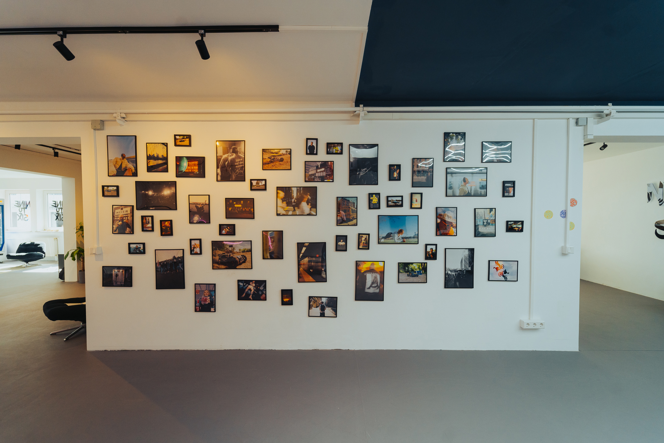 Weiße Wand in einem modernen Raum, an der viele verschiedene gerahmte Fotos und Bilder angeordnet sind.