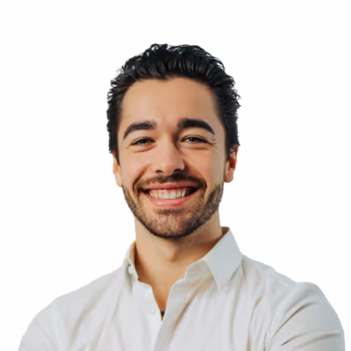 Ein lächelnder junger Mann mit dunklem, gelocktem Haar und Bart, der ein weißes Hemd trägt vor weißem Hintergrund.