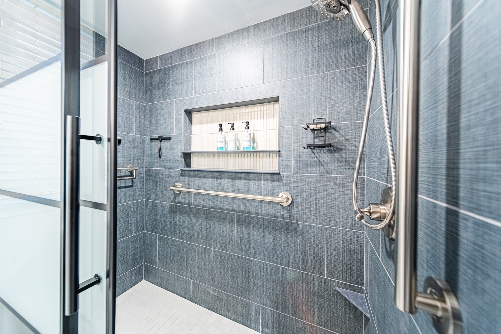 Sliding frosted glass shower door with tiled walk-in shower and grab bars in basement bathroom remodel