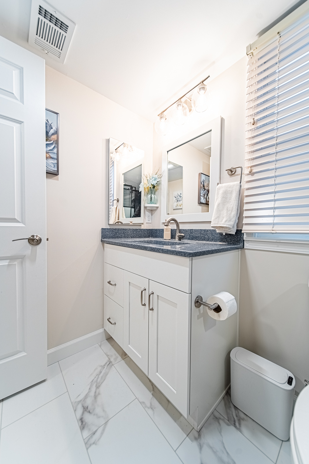 Close-up of vanity cabinet, faucet, and marble-look tile flooring in a bright, updated Lafayette bathroom.