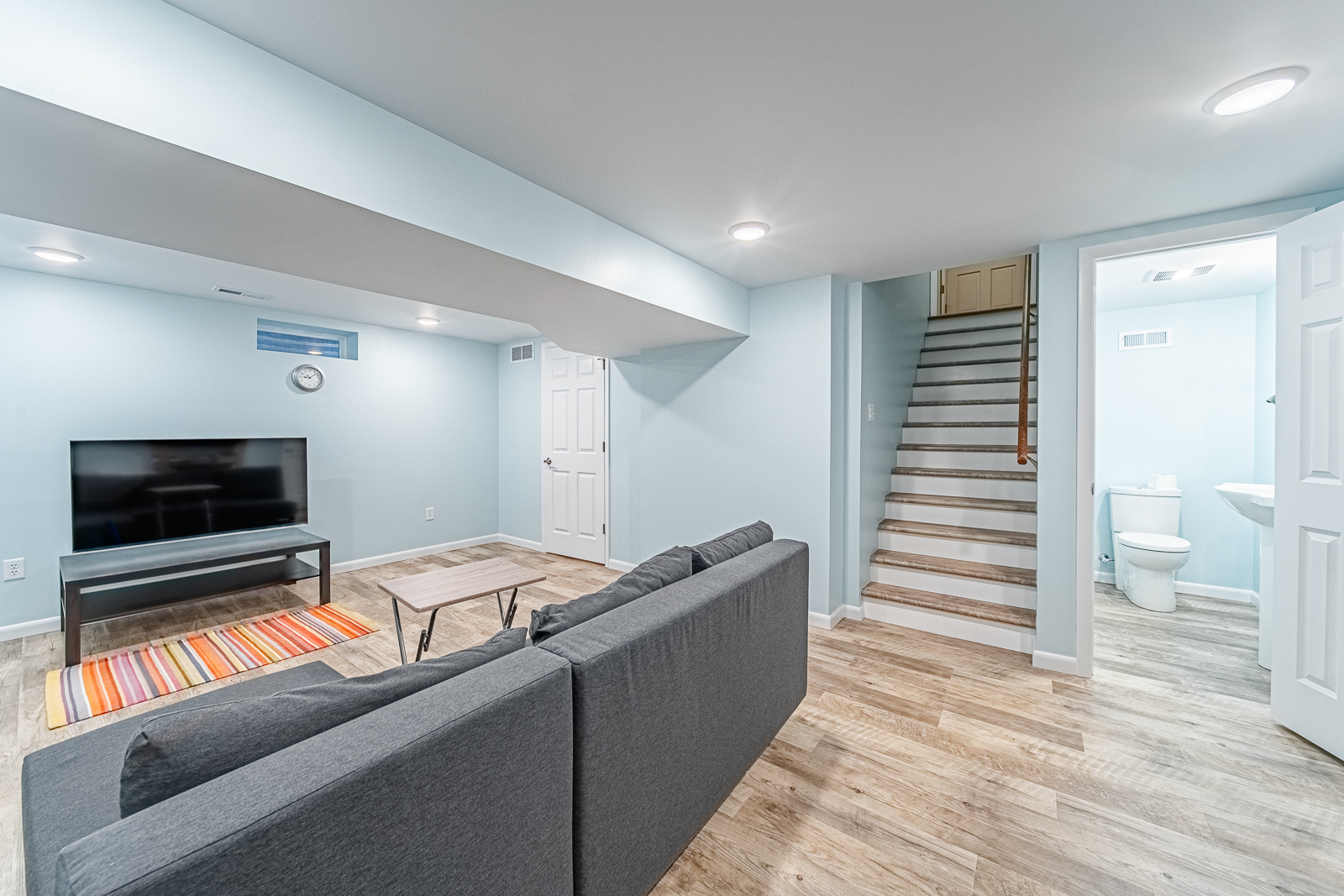 This West Lafayette basement remodel features luxury vinyl plank flooring, added lighting, a sleek half bath, and new drywall-wrapped windows.
