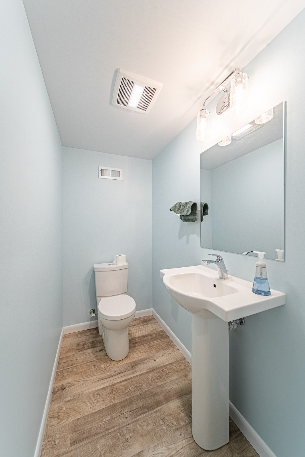Basement powder room with light blue walls, pedestal sink, and toilet.