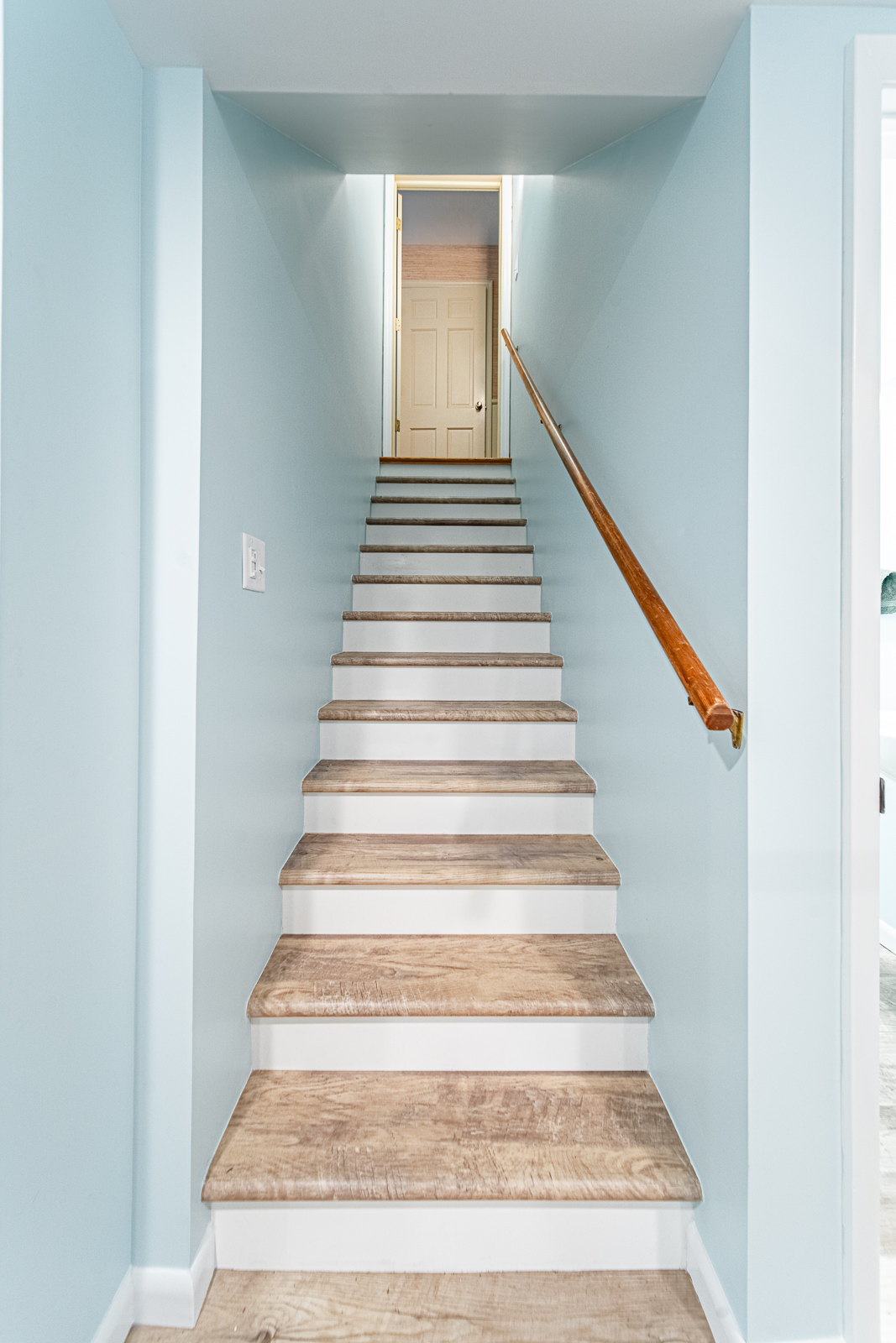 View of the staircase leading from the basement, with wood-look treads and a wood handrail against soft blue walls.