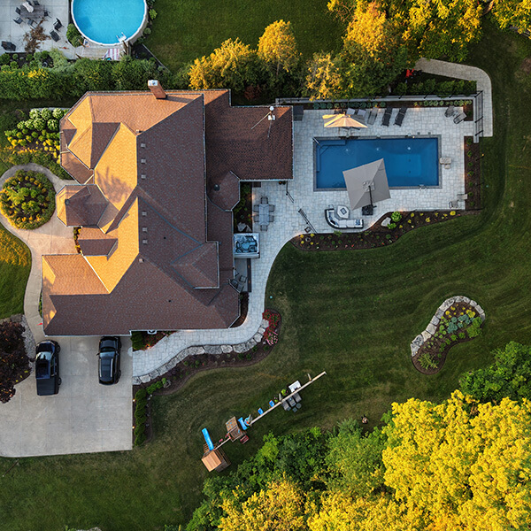 Aerial view of a house with a backyard pool, patio seating, a round pool, and a playground set.