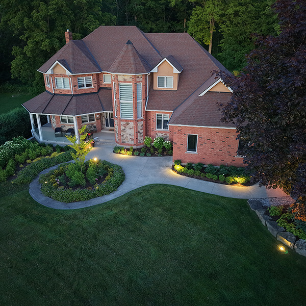 A large brick and stone house with lit pathways and landscaped garden at dusk.