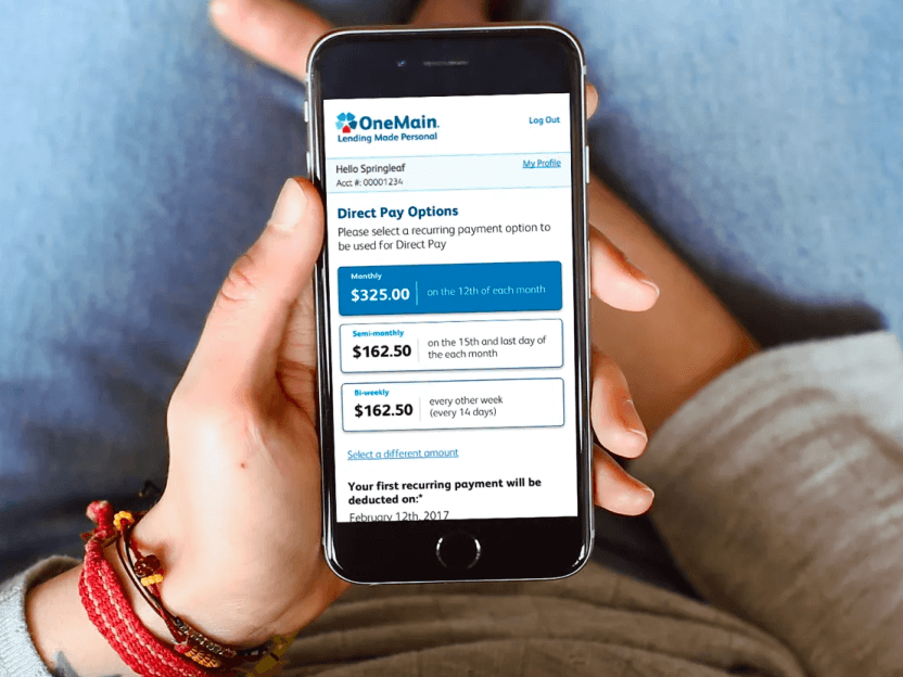 A person holding a cell phone with the OneMain payment UI shown.